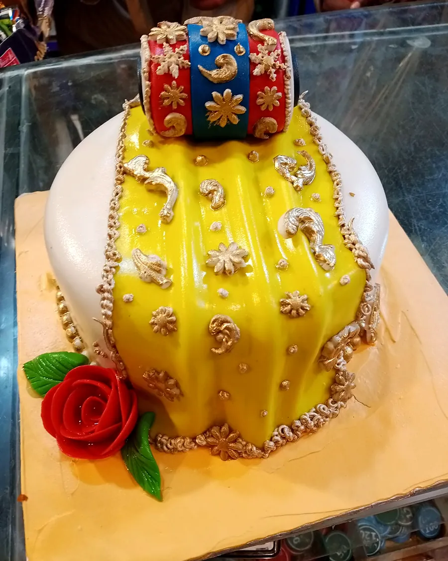 Yellow dholki cake with a gold-trimmed fondant dupatta, a red rose and a dhol on top
