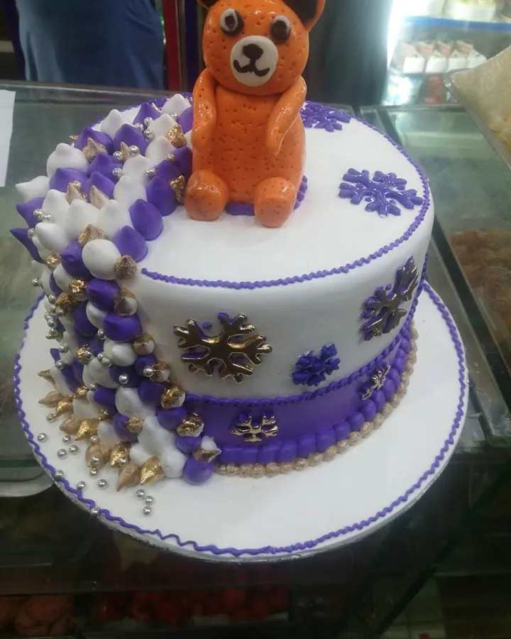 White and purple cake with a teddy bear on top